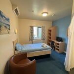 A patient's bedroom with bed, chair and shelves