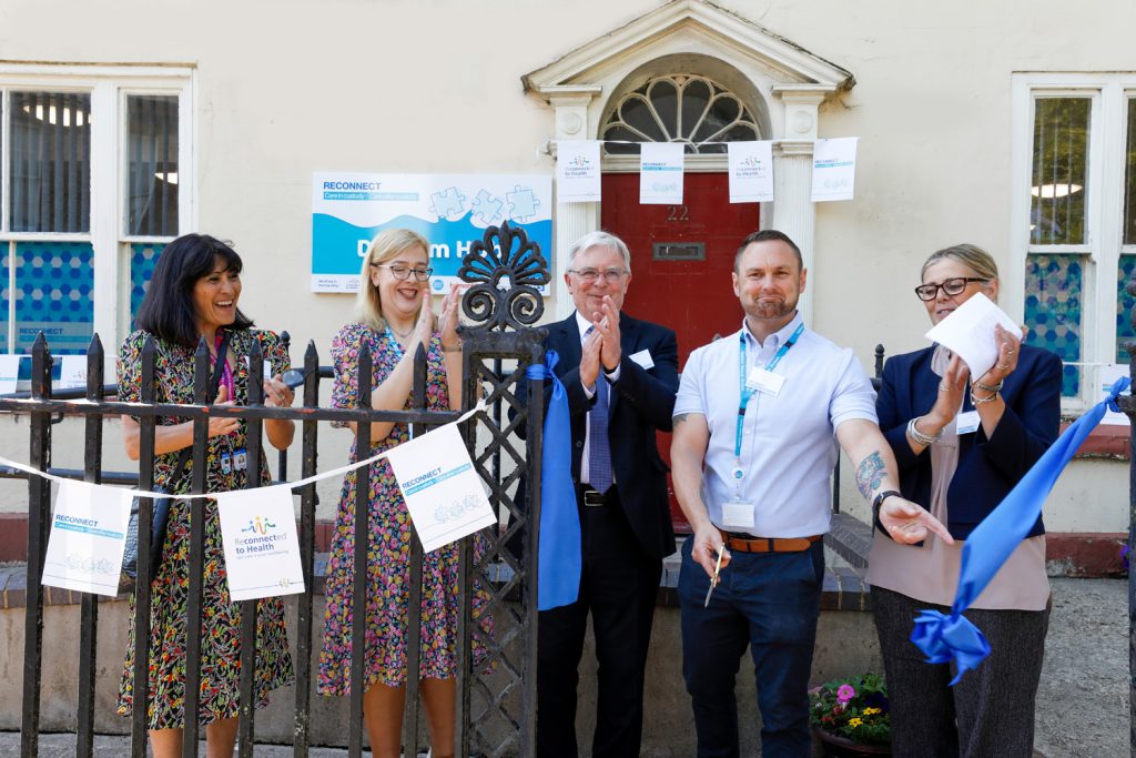 five people stood outside a building having cut a blue ribbon as part of an official opening. 