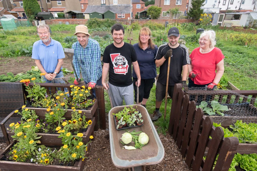 Participants of the Land to Plate Programme stood in thee allotment with their produce