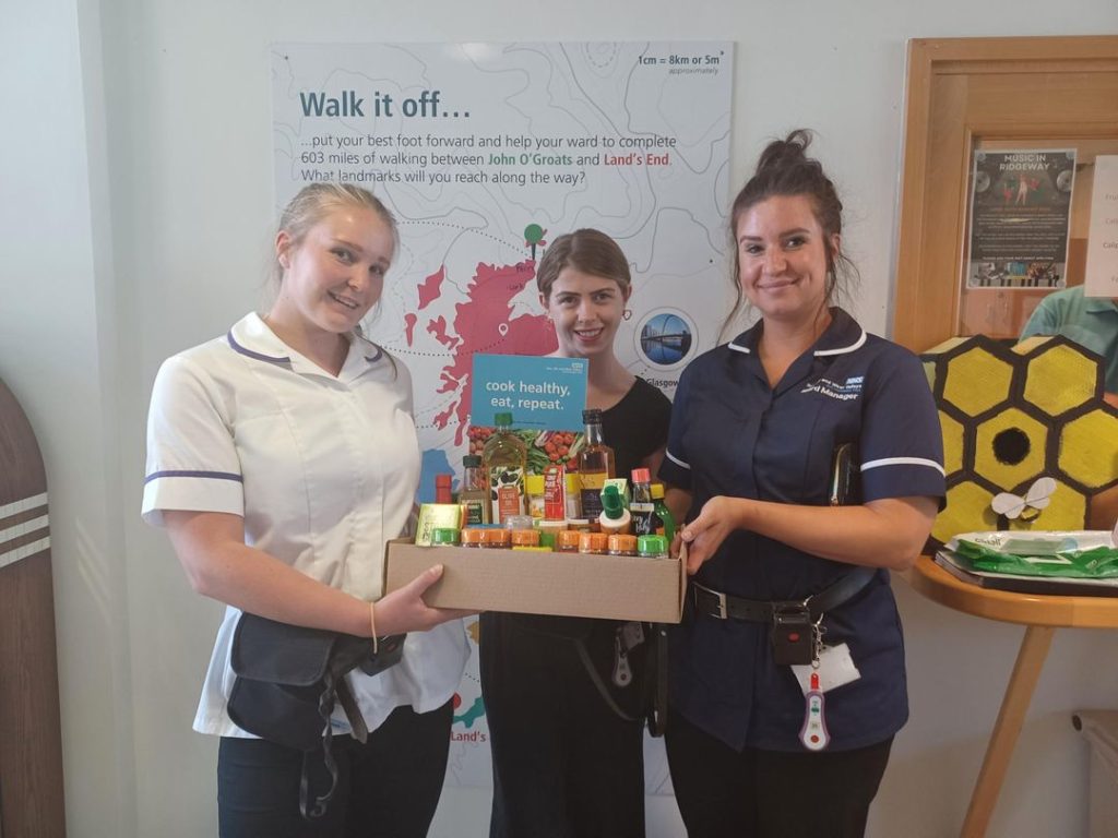 Photo of two staff members smiling with a hamper of food and a cookbook.